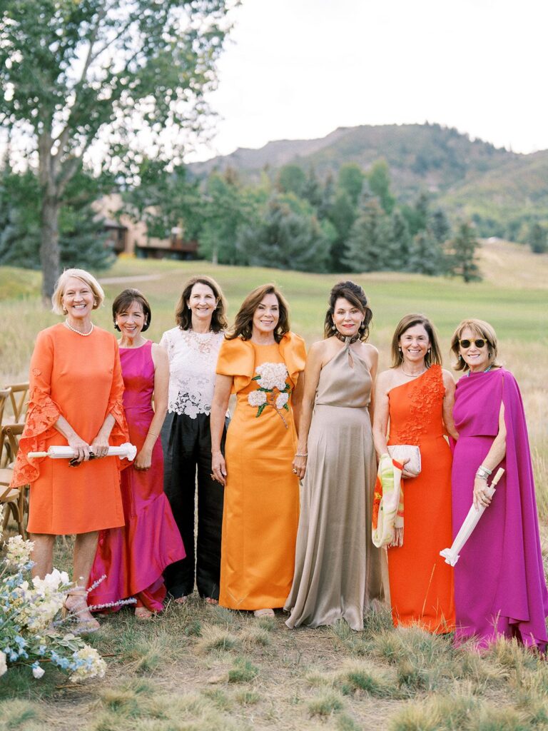 group of women in colorful wedding guest attire at an aspen mountain wedding, bold orange and magenta dresses with mountains behind