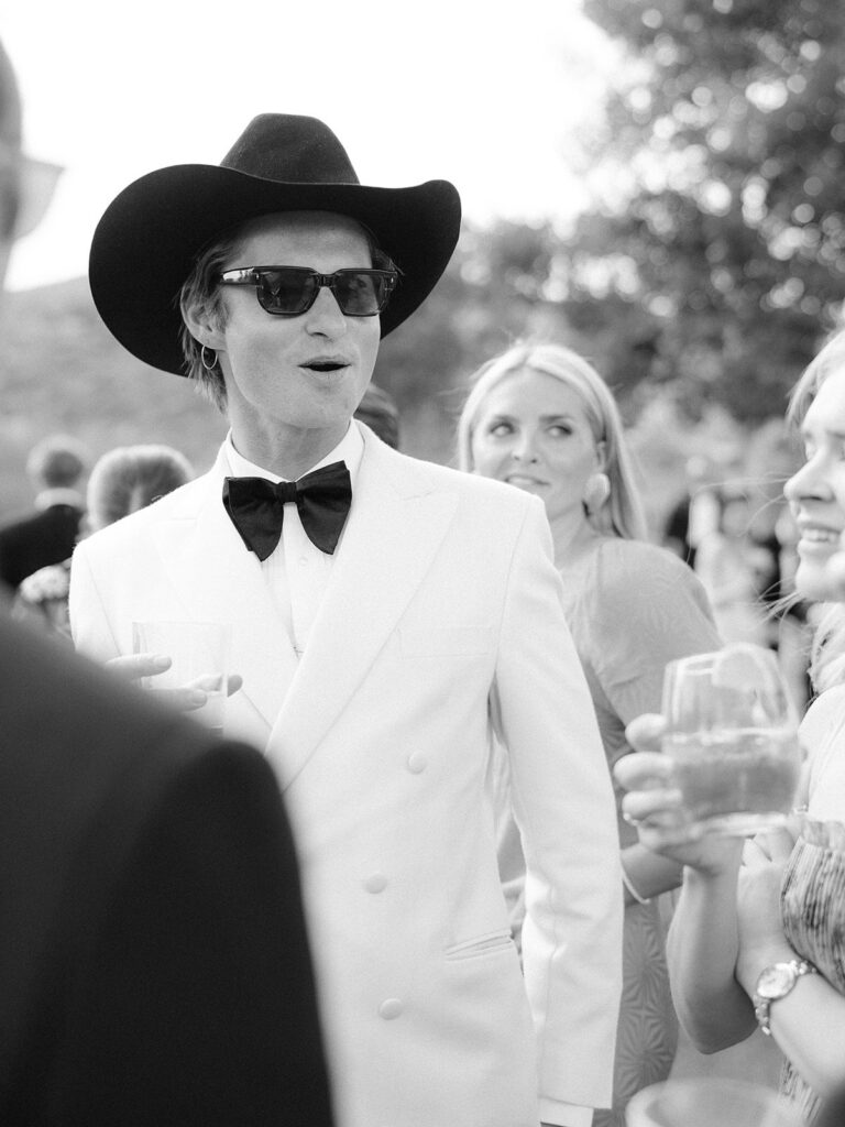 mens western black tie wedding guest attire at an aspen wedding, white double breasted tuxedo with a black bow tie and a cowboy hat